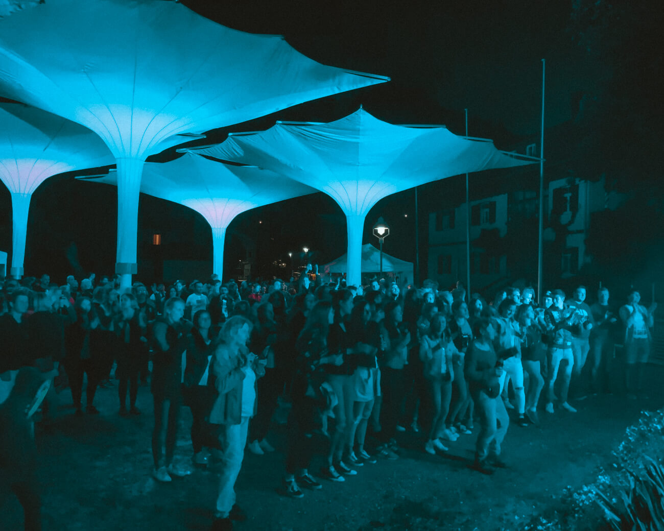 Menschenmenge unter Schirmen blau angeleuchtet von Bühnenlicht
